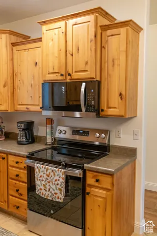 Wood-finish cabinetry with crown molding, stainless steel microwave, stainless steel range, and stone-finish countertops