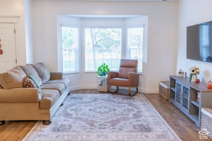 Light wood-finish flooring, white walls, and a bay window with blinds