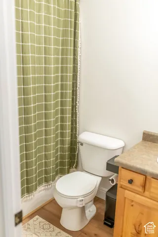 Wood-finish flooring with white baseboards, a white toilet, and a light wood-tone vanity with a countertop