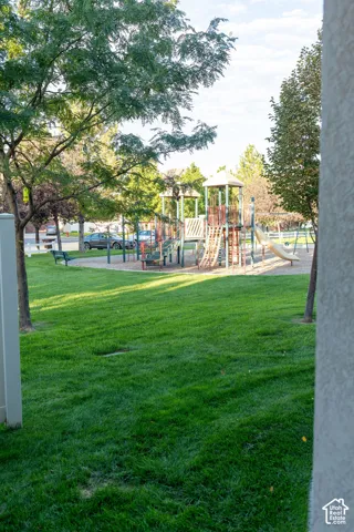 Expansive grassy area with mature trees and a dedicated play structure featuring multiple slides and climbing elements