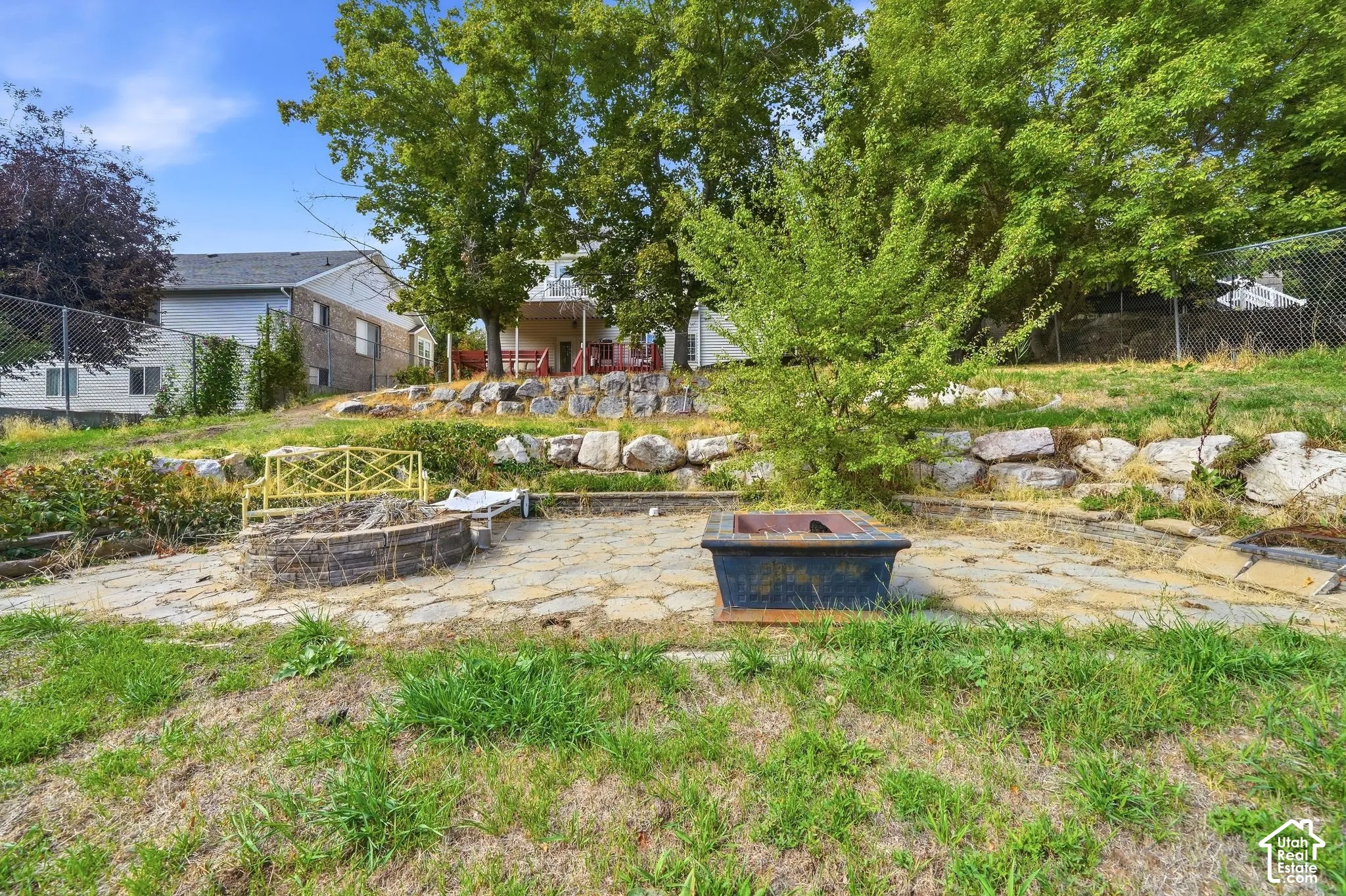 Terraced backyard featuring a stone fire pit, paver patio, natural rock retaining walls, and mature landscaping