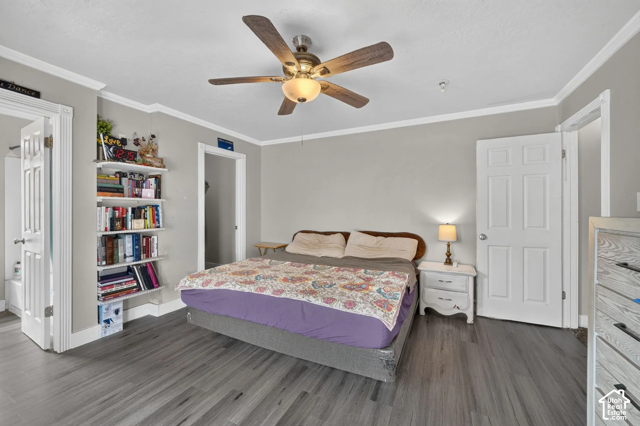 Wood-finish flooring, ceiling fan with integrated lighting, built-in shelving, crown molding, and a paneled interior door