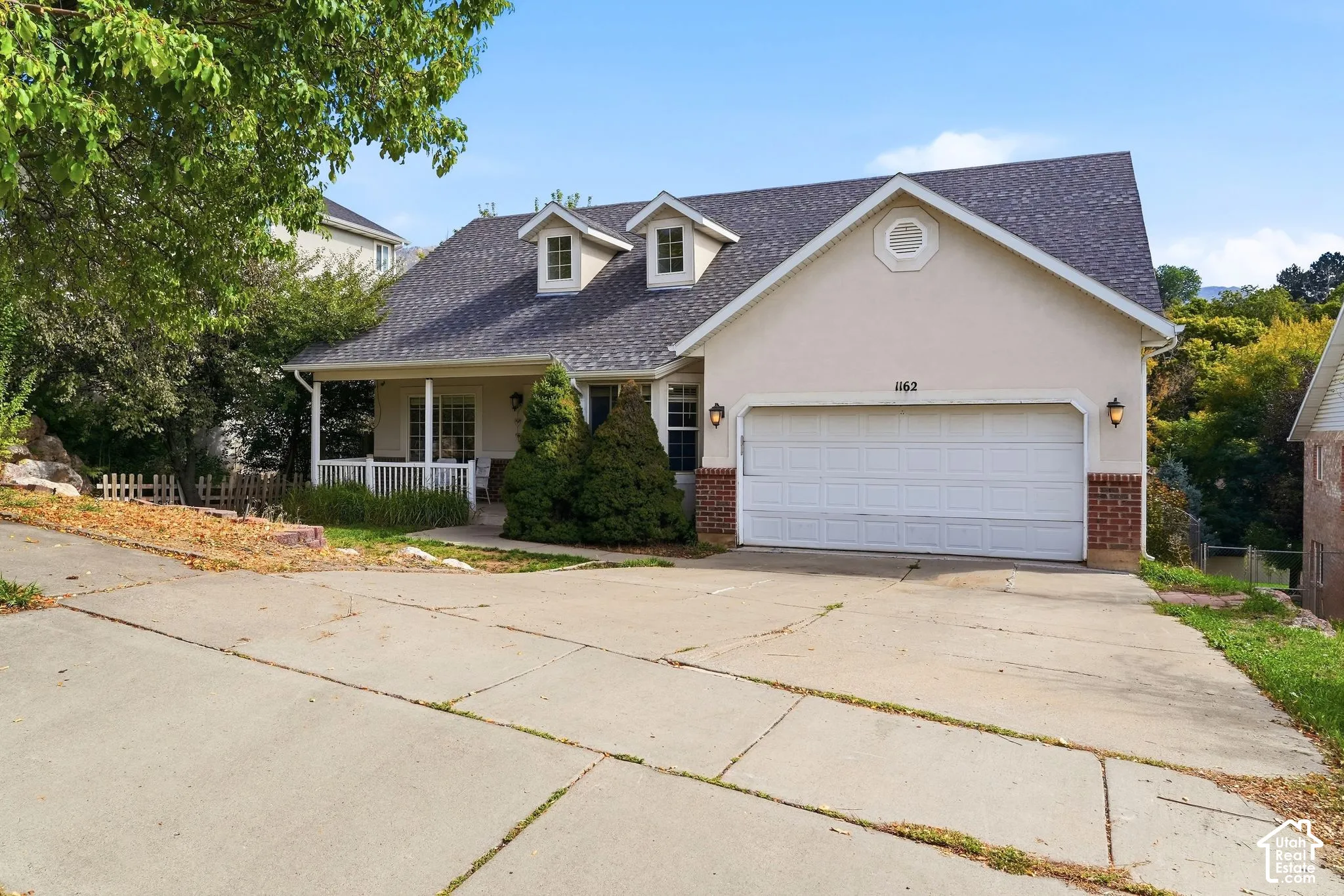 Front exterior featuring a covered porch with white columns, attached two-car garage, and dormer windows