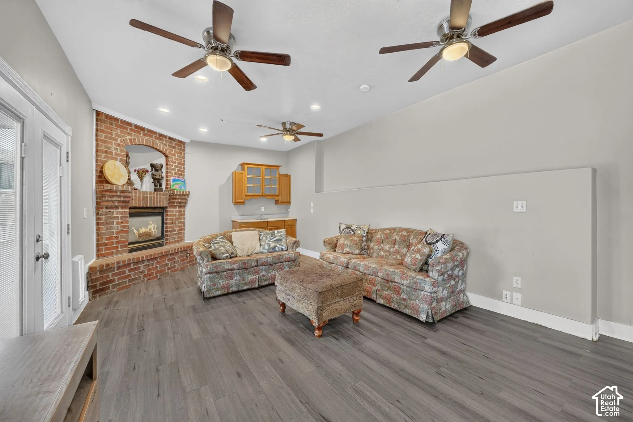 Brick fireplace with an arched opening, wood-finish flooring, two ceiling fans with lighting, recessed lighting, and built-in cabinetry