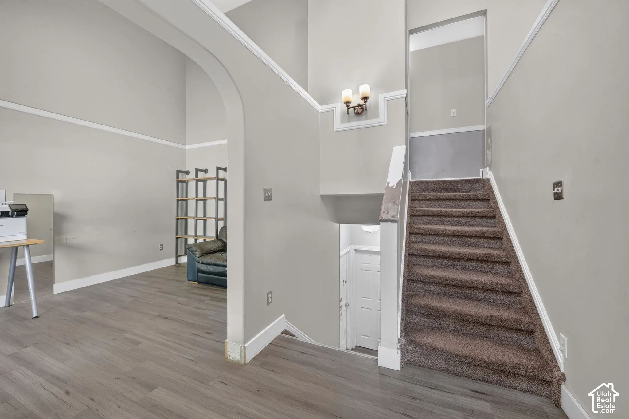 Vaulted ceilings, archway entry, wood-finish flooring, staircase with carpeted treads, and wall-mounted light fixture