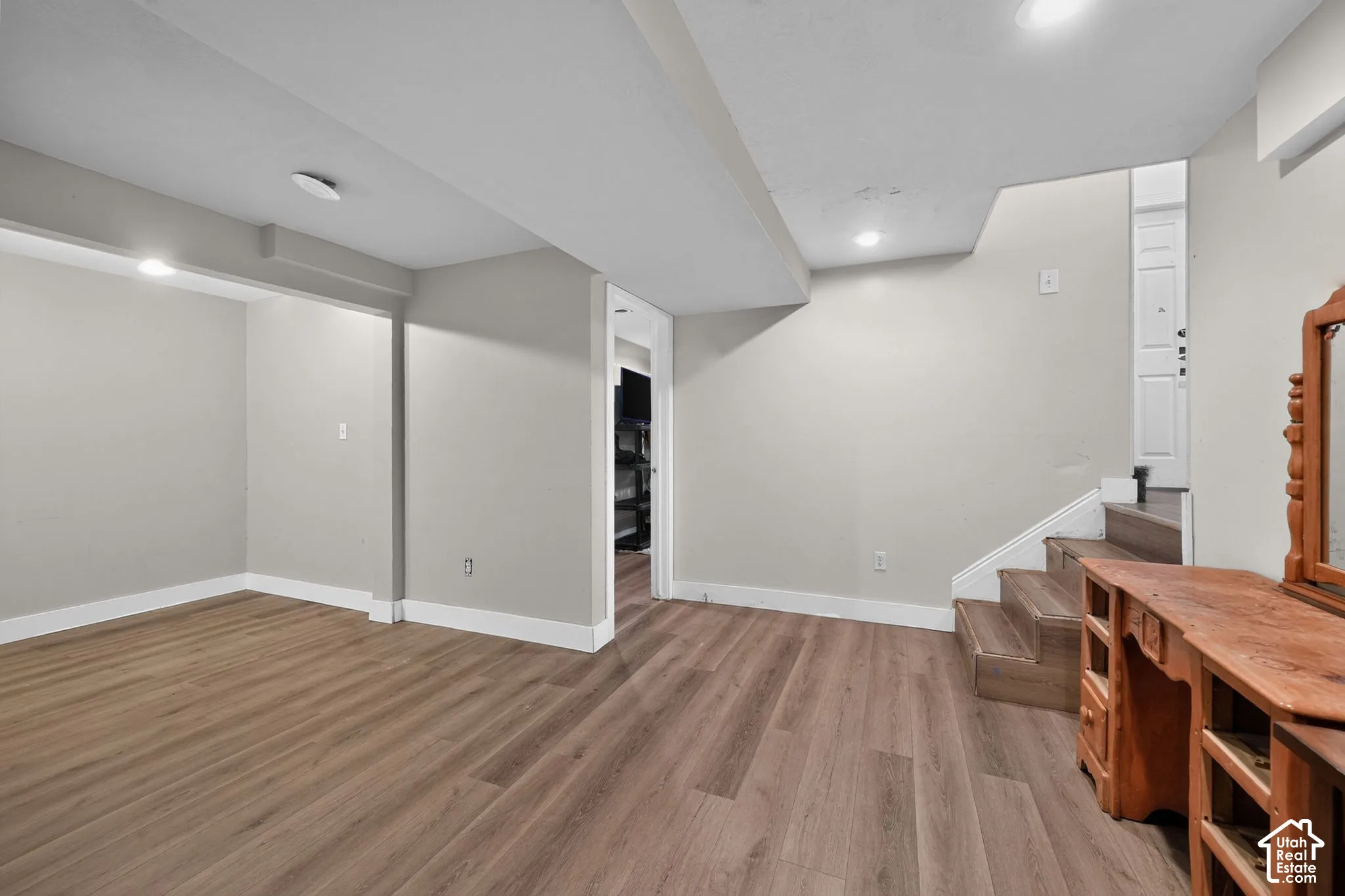Wood-finish flooring, recessed ceiling lighting, light gray wall paint, and white trim accents