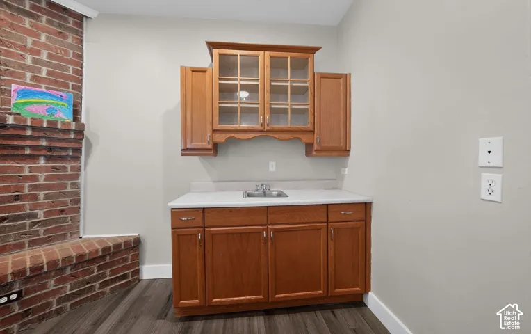 Brick fireplace, wood-finish flooring, built-in cabinetry, upper display cabinet with glass inserts, and a built-in sink with a countertop