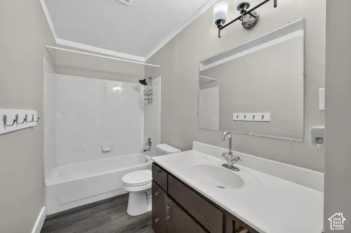 White bathtub with an integrated shower, dark wood-finish vanity with a white countertop and integrated sink, chrome-finish faucet, wall-mounted mirror, and wood-finish flooring