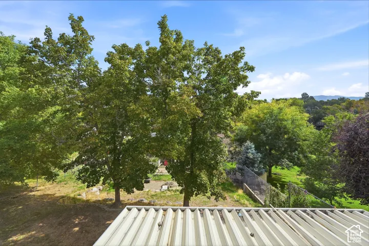 Corrugated metal roof with a backdrop of mature trees, expansive green landscaping, and distant hills under a clear sky