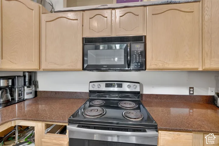 Kitchen featuring light wood-finish cabinetry, a built-in microwave, and a black and stainless steel electric range