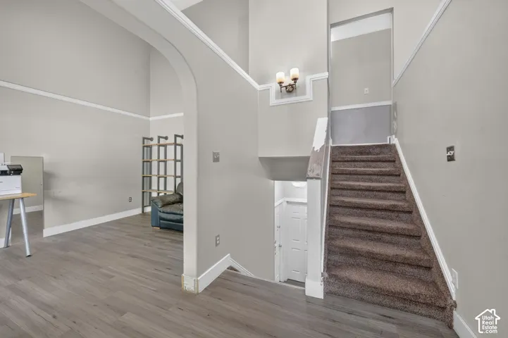 Vaulted ceilings, archway entry, wood-finish flooring, staircase with carpeted treads, and wall-mounted light fixture