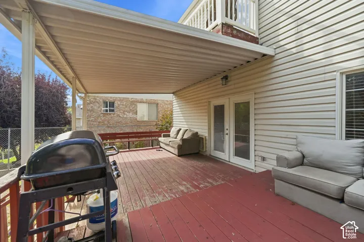 Expansive covered deck featuring a white patio cover, red wood-finish flooring, and white French doors