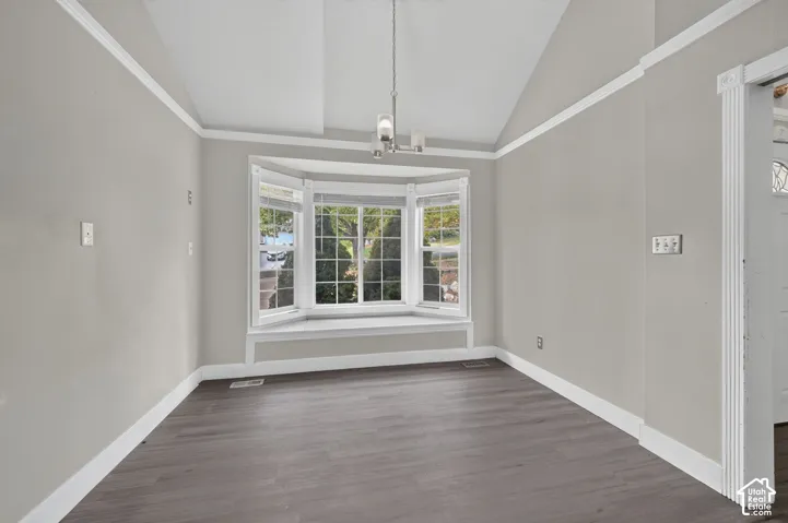 Vaulted ceiling with crown molding, bay window with integrated sill, wood-finish flooring, and a contemporary chandelier