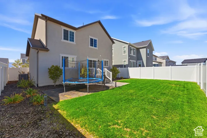 Expansive backyard featuring a manicured lawn, established landscaping, and a white privacy fence