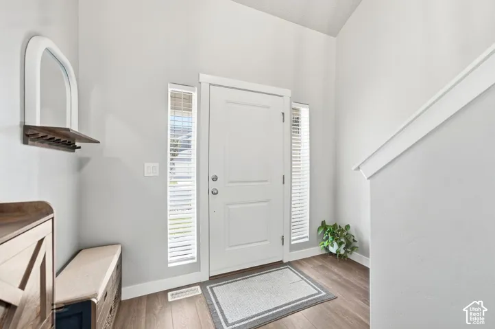 Entryway featuring wood-finish flooring, a white front door with sidelights, and a staircase with a white handrail