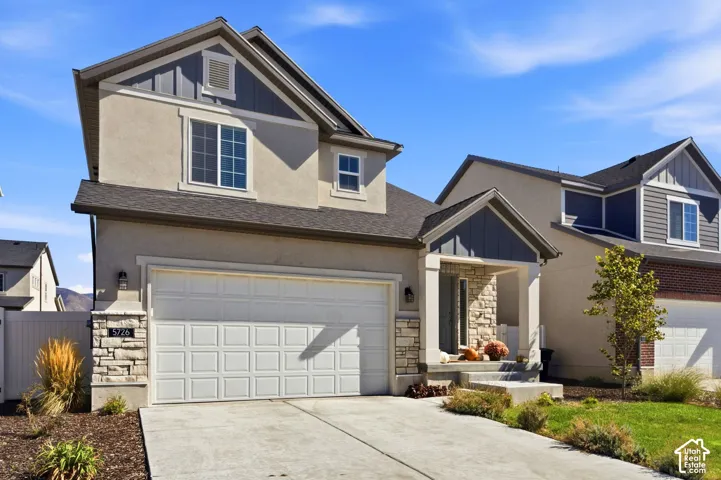 Stone veneer accents, stucco exterior, covered front entry, attached garage, and architectural shingles