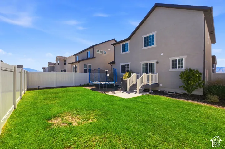 Expansive grassy yard with a white vinyl fence, concrete patio, and a staircase with white railings