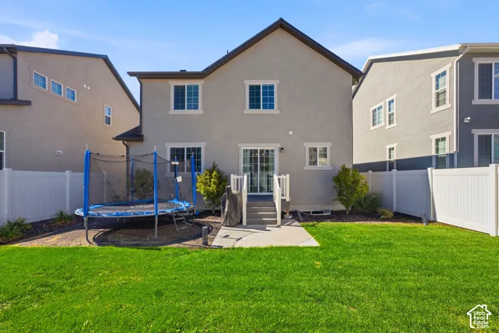 Expansive green lawn, white privacy fencing, concrete patio, rear exterior with multiple windows, and a sliding glass door