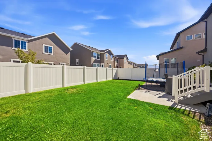 Expansive green lawn with a white privacy fence, concrete patio, and exterior stairs with white railings