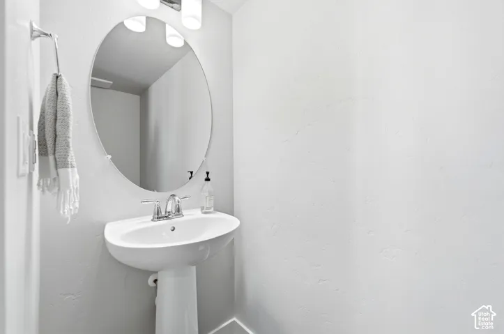 Pedestal sink with chrome faucet, oval mirror, and wall-mounted light fixture