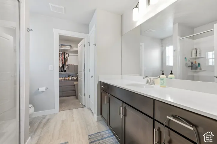 Spacious bathroom featuring a dual vanity with a white countertop and dark wood-finish cabinetry, wood-finish flooring, and a walk-in shower with a glass enclosure