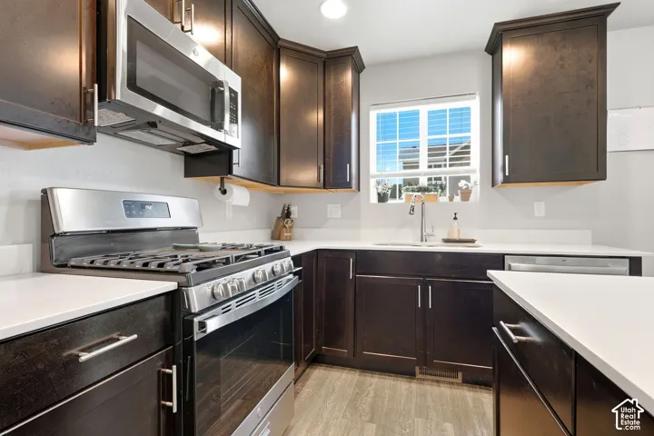 Kitchen featuring dark wood-finish cabinetry, stainless steel appliances, solid surface countertops, a stainless steel sink, and wood-finish flooring