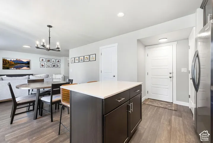 Wood-finish flooring throughout, kitchen island with dark cabinetry and light-toned countertop, modern chandelier, white paneled door, and recessed lighting