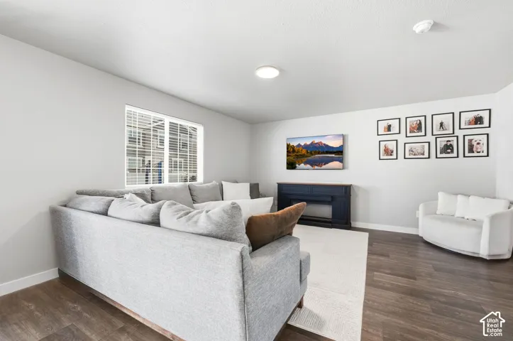 Spacious living area featuring wood-finish flooring, light-toned walls, a large window with blinds, and recessed lighting