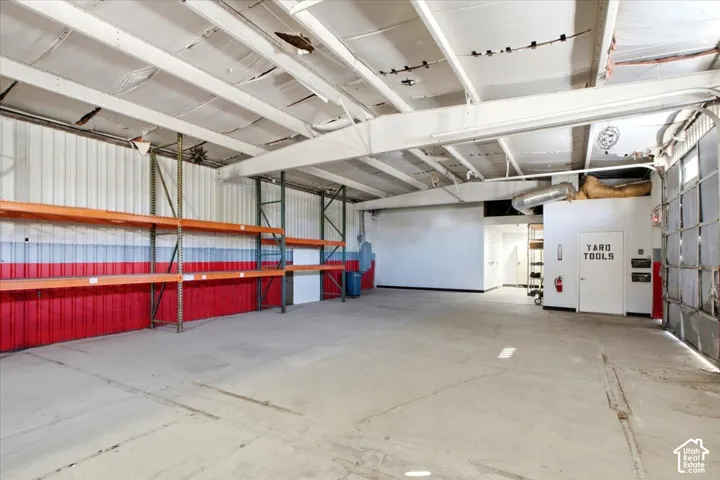 Concrete flooring, exposed ceiling beams, built-in shelving, white wall panels, and a roll-up door