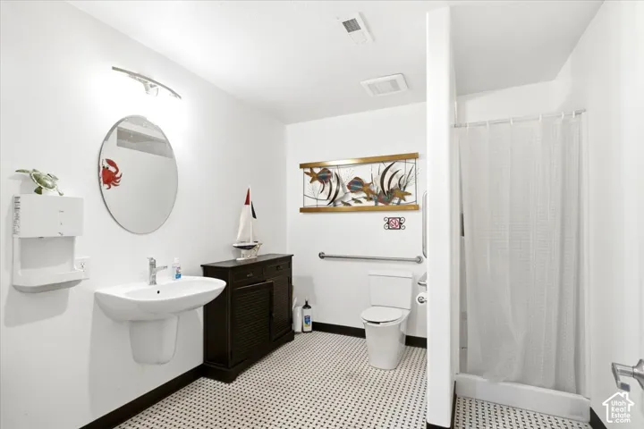 White pedestal sink with a chrome faucet, round wall mirror, and an adjacent dark wood-finish cabinet