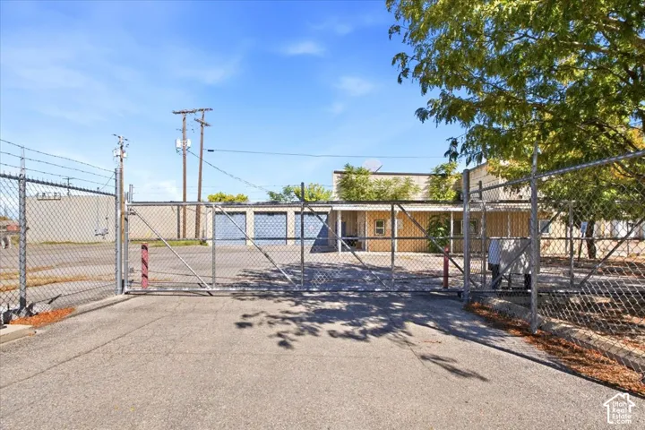 Gated entry with chain-link fencing, asphalt drive, and mature trees
