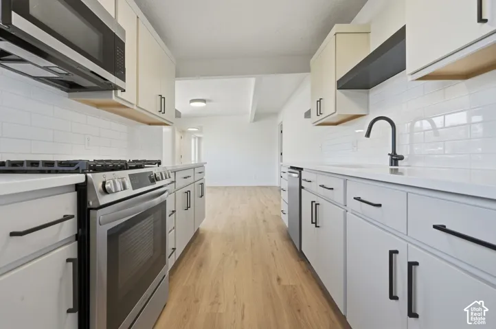 Modern kitchen featuring white cabinetry, subway tile backsplash, stainless steel appliances, matte black fixtures, and wood-finish flooring