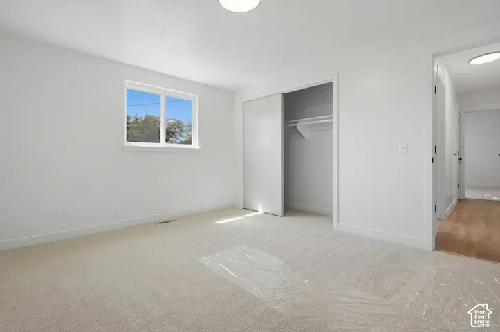 Neutral tone carpeted flooring, white walls, built-in closet with sliding doors, and a window with white trim