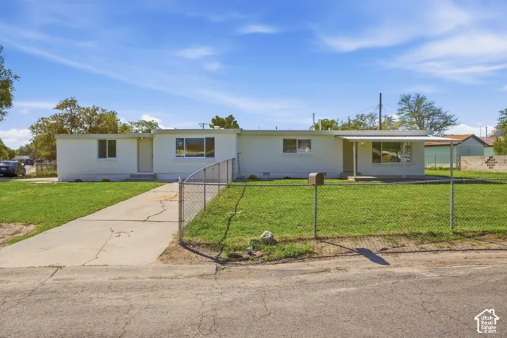 White stucco exterior, chain-link fencing, mature landscaping, front yard, paved driveway