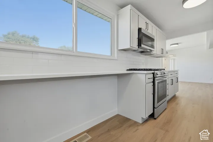White cabinetry with matte black hardware, stainless steel appliances, white subway tile backsplash, light-toned wood-finish flooring, and white countertops