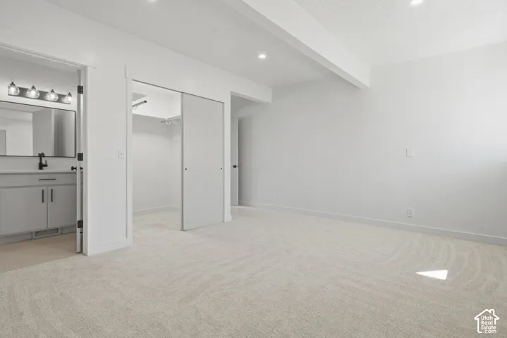 Plush carpet flooring with recessed lighting, an open closet with sliding doors, and an attached bathroom featuring a single vanity and wall-mounted light fixture