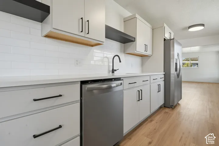 Modern kitchen featuring white cabinetry with matte black hardware, stainless steel appliances, white subway tile backsplash, white countertops, and wood-finish flooring