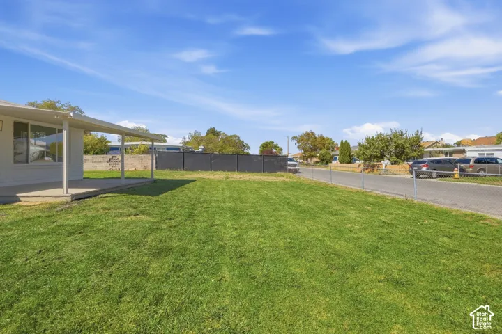 Expansive grassy yard with a covered concrete patio and a chain-link fence