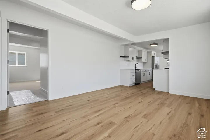 Wood-finish flooring, white walls, recessed kitchen with white cabinetry, stainless steel dishwasher, and a black faucet