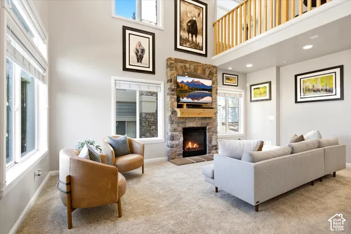 Two-story living area featuring a stone fireplace with a wood mantle, high ceilings, multiple windows, and a loft overlook with a wood railing