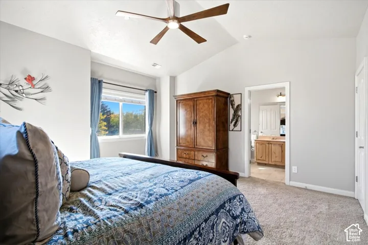 Vaulted ceiling with ceiling fan, recessed window, light gray walls, carpeted flooring, and a doorway to a bathroom with a wood-finish vanity