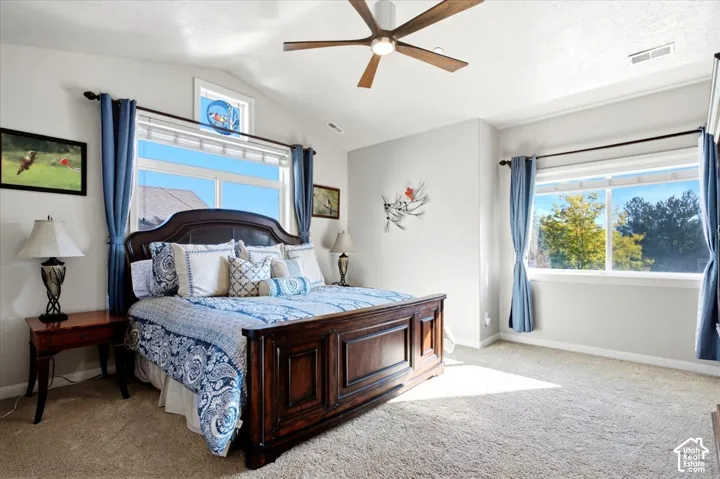 Vaulted ceiling with a ceiling fan, multiple windows, and light-colored carpeting