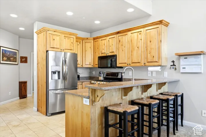 Kitchen featuring wood cabinetry, stainless steel appliances, recessed lighting, a breakfast bar, and tile flooring