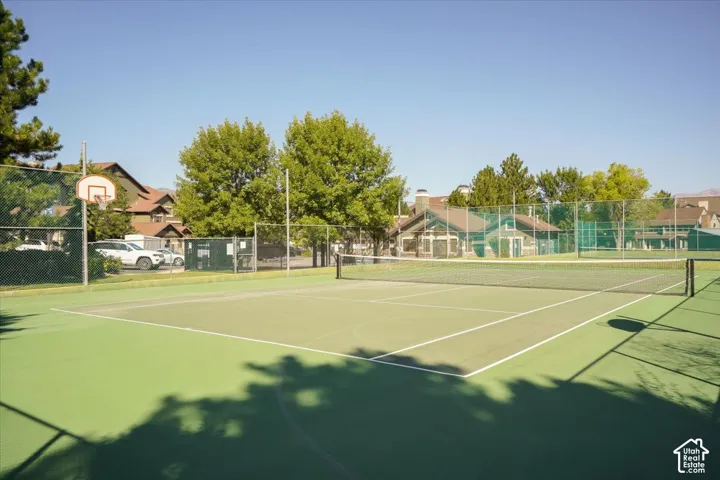 Outdoor tennis court with a basketball hoop and chain-link fencing