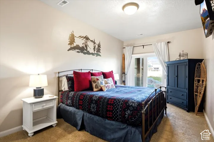 Carpeted bedroom featuring a metal bed frame, white nightstand with a drawer, and double glass doors