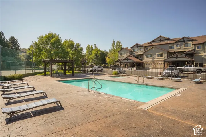 Outdoor swimming pool with patterned concrete decking, adjacent to a tennis court and a pergola-covered patio