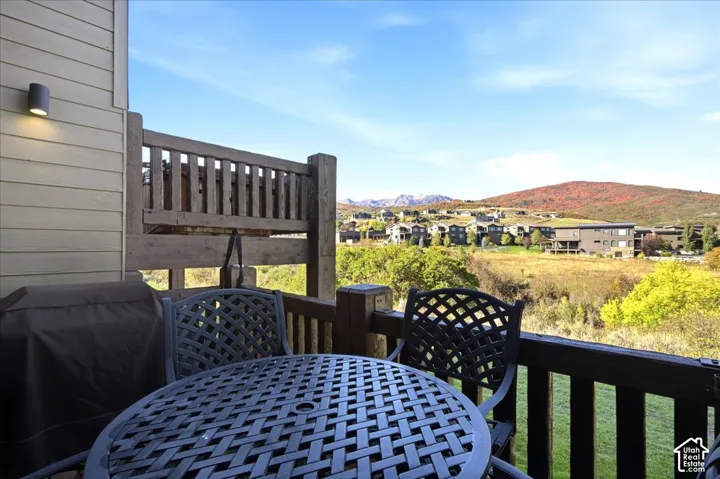 Private balcony with wood railing, featuring a wall-mounted light fixture and scenic distant hills