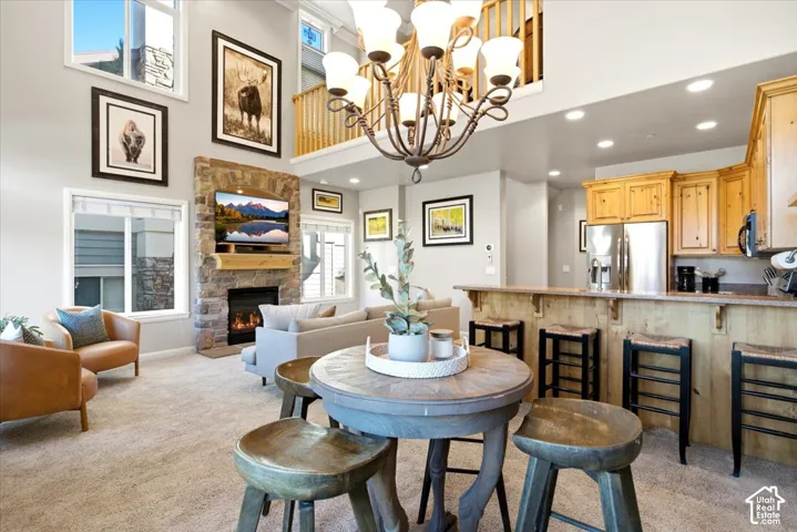 Two-story stone fireplace with natural wood mantel, two-story windows, open-concept kitchen with wood cabinetry, stainless steel refrigerator, and recessed lighting