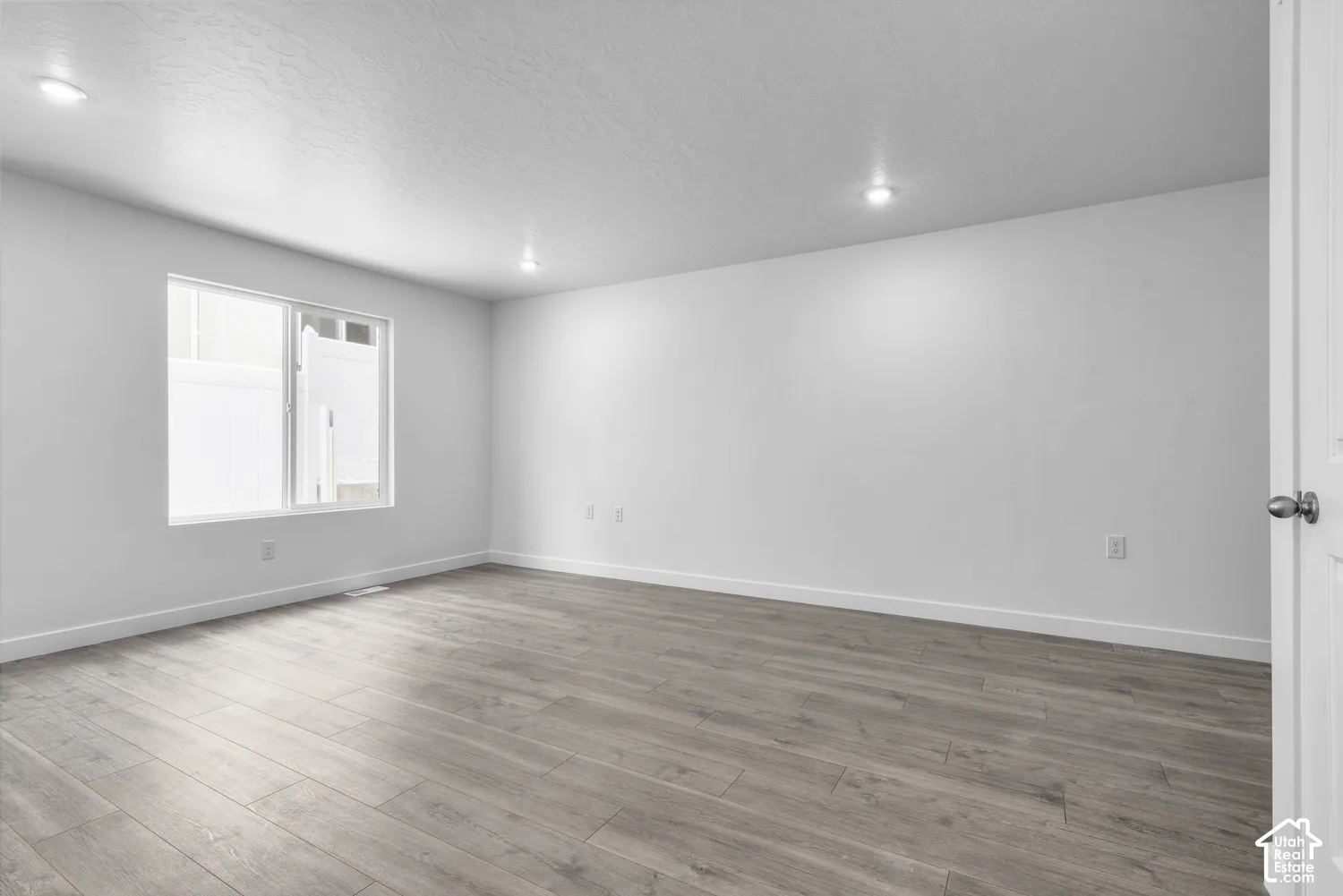 Recessed lighting illuminates the expansive room featuring wood-finish flooring and a bright window