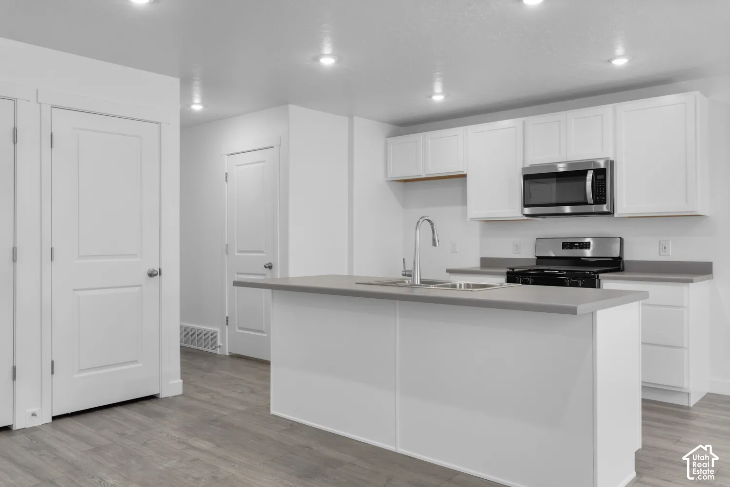 Kitchen featuring an island with an undermount sink, white cabinetry, stainless steel appliances, and wood-finish flooring